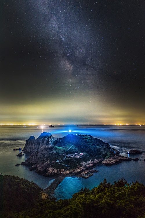「第１７回国立公園写真公募展」の最優秀賞受賞作品。夜明け、小毎勿島で操業する船の光、灯台の光、星空が美しい。