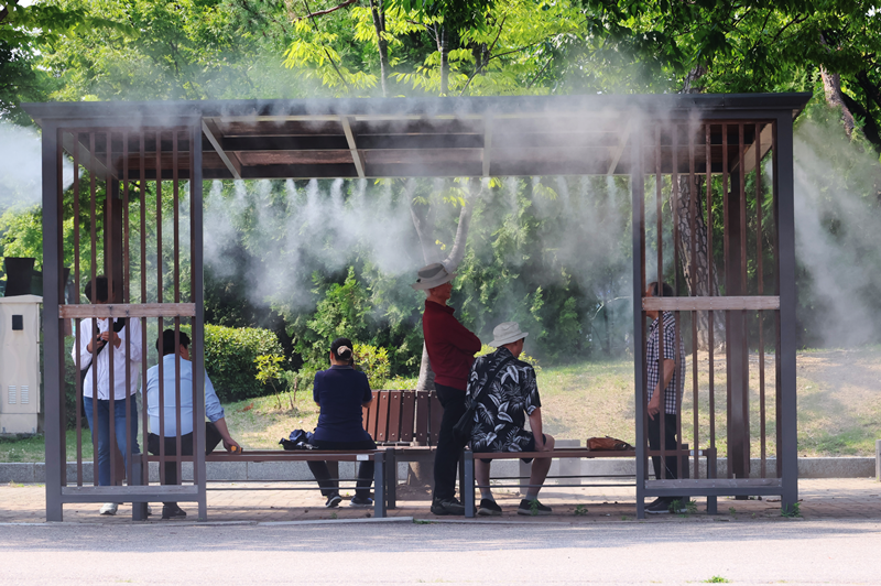 暑さを避けるために、公園に設置された「クーリング・フォグ」。写真は、「クーリング・フォグ」の下で休息をとる市民の様子＝６月、ソウル・汝矣島、聯合ニュース