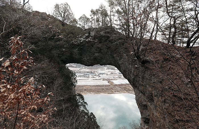 嶋潭三峰展望台の左を登ると絶対見逃してはいけない丹陽の絶景、「石門」が姿を現す。雲橋の形をしている石柱の向こうには南漢江と穏やかな村の風景が一幅の絵のように広がる