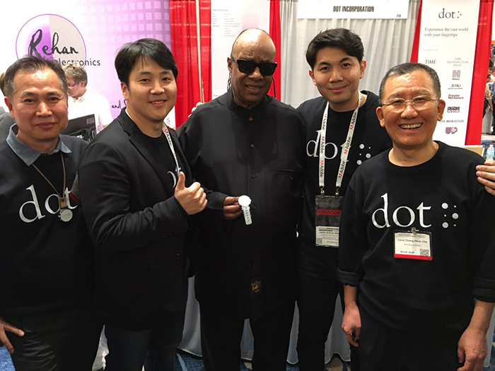 昨年3月に行われた福祉機器展示(CSUN)で歌手のスティーヴィー・ワンダー(中央)とキム・ジュユン代表(左から2番目)などドットの社員たちが記念撮影をしたときの様子。ワンダーはこの日、ドットウォッチと事前契約を結び関心と賞賛を送った