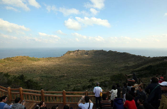 성산일출봉 정상에 오른 사람들이 주변 풍경을 사진에 담고 있다. 성산일출봉 정상에서는 가운데 넓은 분지가 초원처럼 펼쳐져 있는 분화구의 모습을 한 눈에 볼 수 있다.