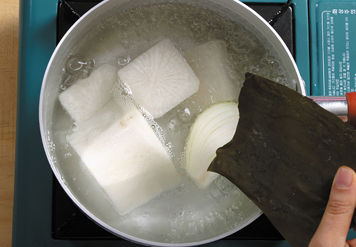 물을 넣은 냄비에 무와 양파를 넣고 끓이다가 다시마를 넣고 불을 끈다.