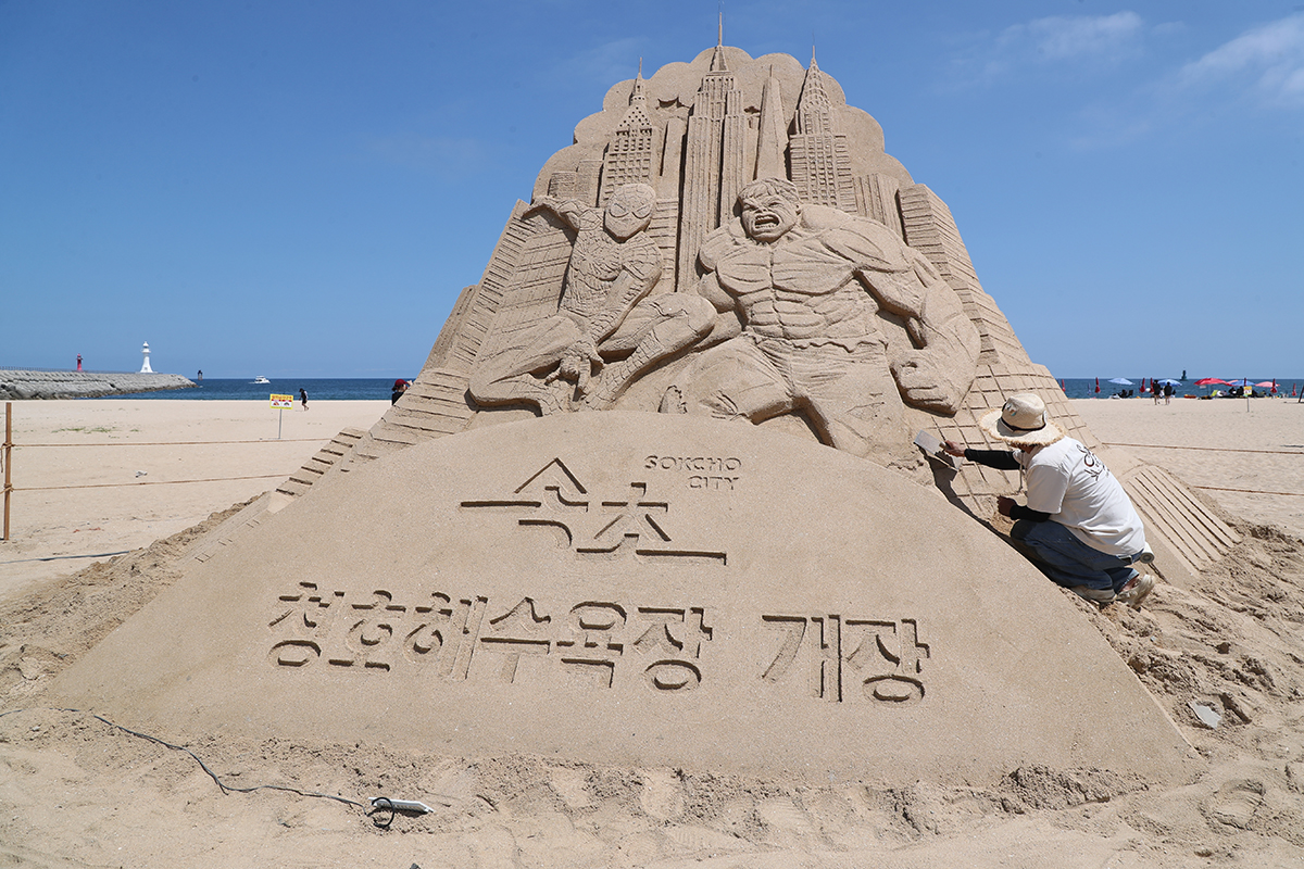 ５日、江原道・束草市のチョンホ海水浴場の砂浜で、スパイダーマンとハルクの砂像作品の設置作業が行われている。